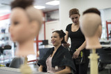 Hairdresser cuts and comb young woman hair in hair school near to mannequin