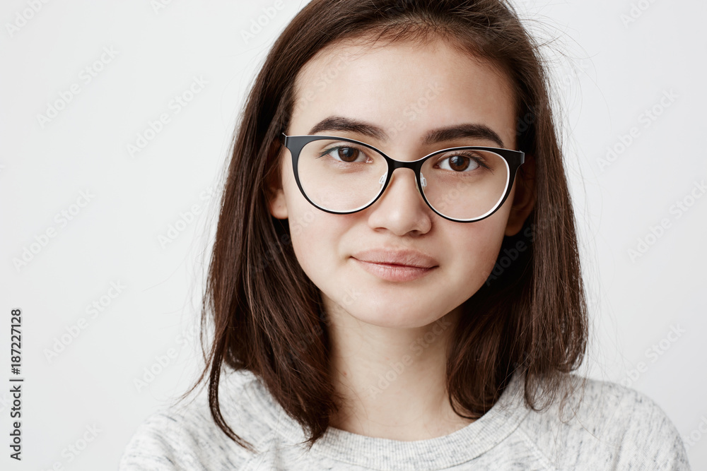 Close-up portrait of stylish dark-haired beautiful teenage girl with trendy haircut dressed in t-shirt, looks at camera, wears trendy eyewear, smiles gently. People lifestyle youth and beauty Close-up portrait of stylish dark-haired beautiful teenage girl with trendy haircut dressed in t-shirt, looks at camera, wears trendy eyewear, smiles gently. People lifestyle youth and beauty