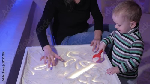 A young mother plays with her son in a salt room. Together they draw patterns on a luminous table.