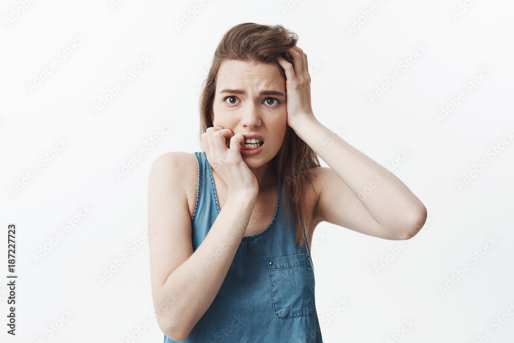 Isolated portrait of beautiful unhappy young caucasian student girl with dark long hair gnawing hands, holding forheand, looking aside with scared expression. Girl being frightened of horror movie in Isolated portrait of beautiful unhappy young caucasian student girl with dark long hair gnawing hands, holding forheand, looking aside with scared expression. Girl being frightened of horror movie in