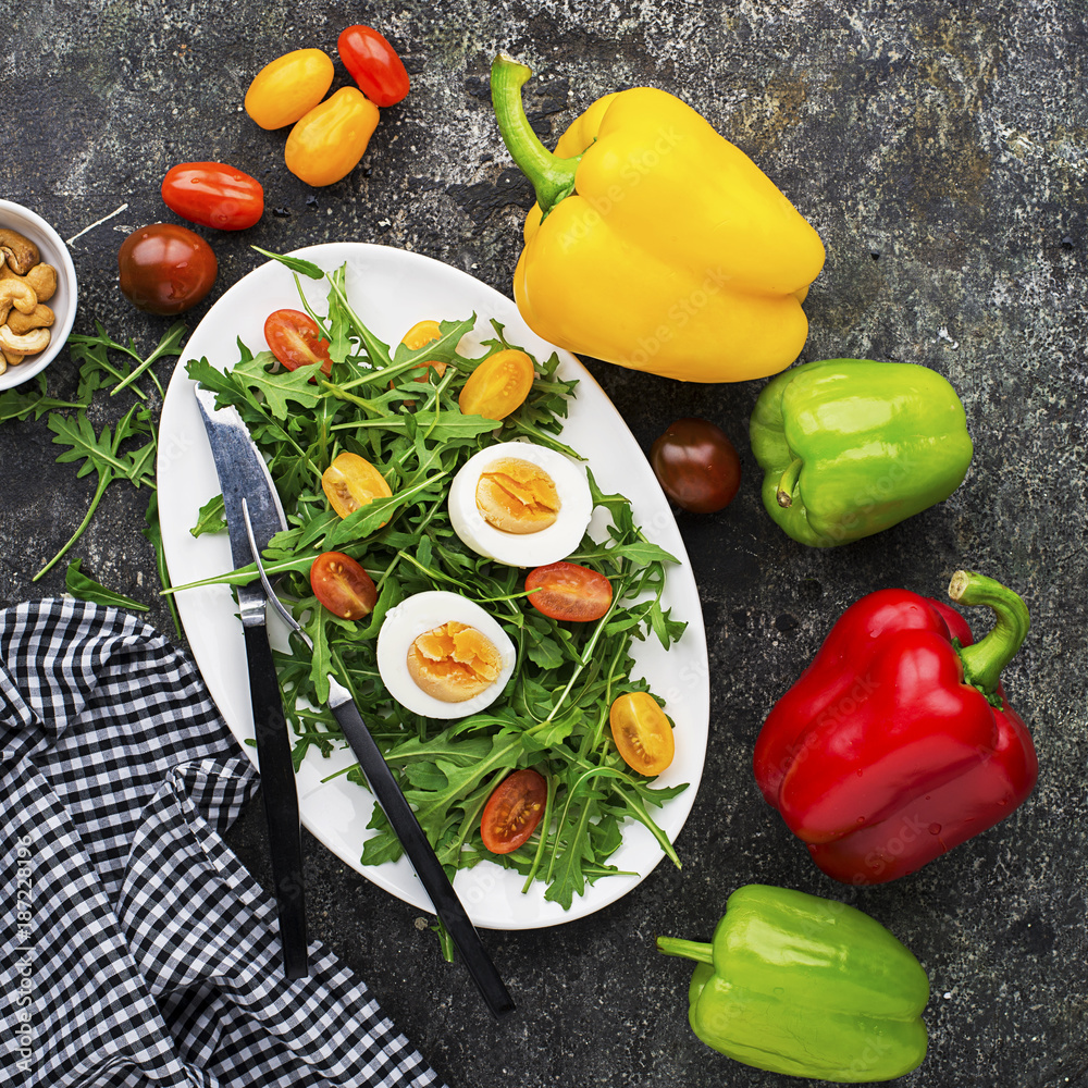 Easter spring salad with fresh vegetables: tomatoes, arugula, egg, nuts and croutons on a gray grunge background. Top view..