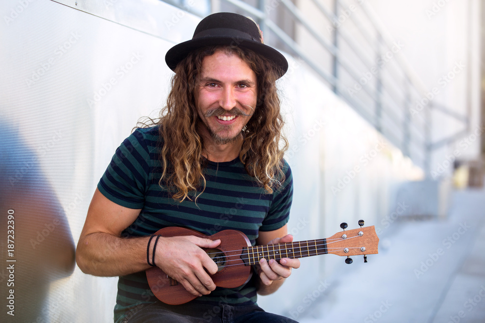 Friendly hipster man with warm personality smiling and playing a ukulele  guitar Stock Photo | Adobe Stock