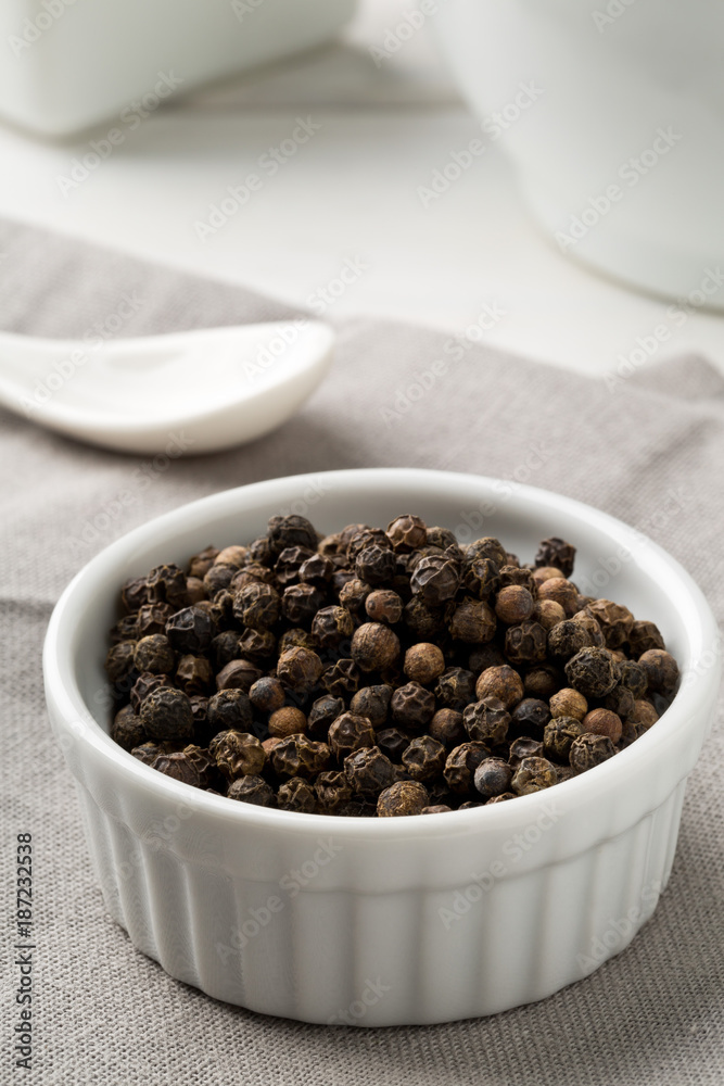 Raw, natural, unprocessed black pepper peppercorns in white bowl Raw, natural, unprocessed black pepper peppercorns in white bowl