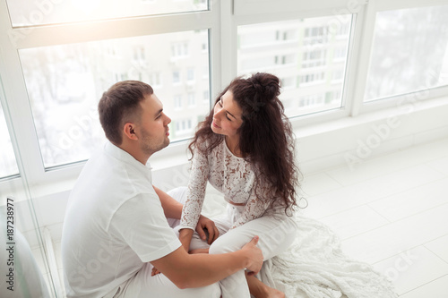 Happy couple or marriage in their new home sitting near the window and hugging together