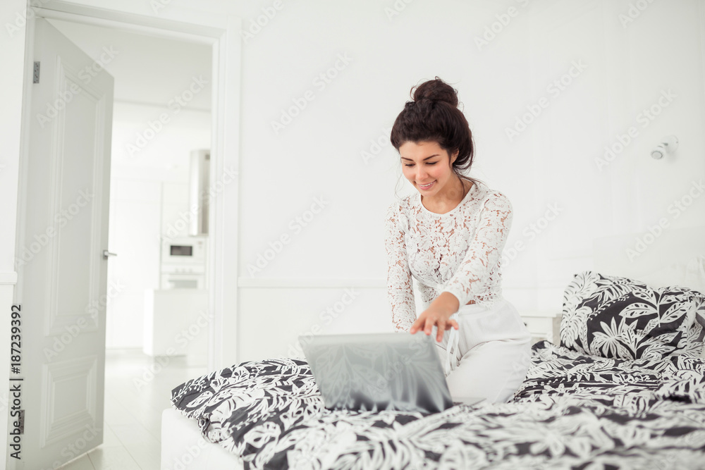 Young woman working with laptop at home, online business. Smiling woman sitting on bed, relaxing, browsing internet or online shopping, free time at home. Young woman working with laptop at home, online business. Smiling woman sitting on bed, relaxing, browsing internet or online shopping, free time at home.