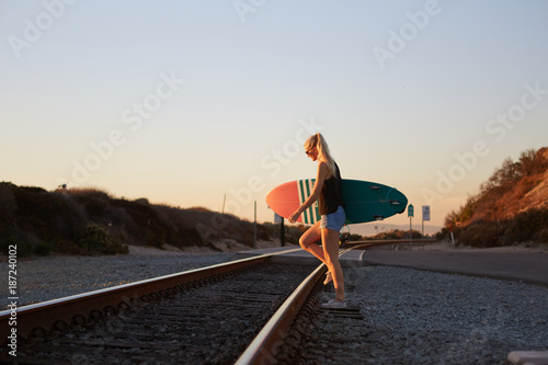 blonde surfer girl walks on railway