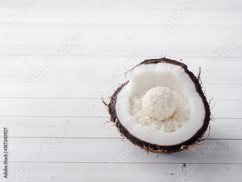 Half of the fresh organic coconut with Coconut and chocolate candy inside on wooden background