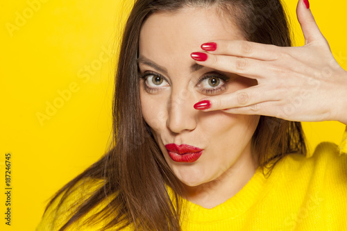 beautiful woman in a yellow blouse, peeking trhrough her fingers on a yellow background