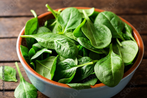 Fresh spinach leaves in bowl on rustic wooden table. Selective focus.