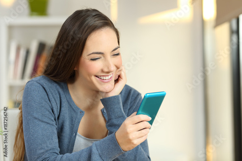 Happy woman reading text in a smartphone at home