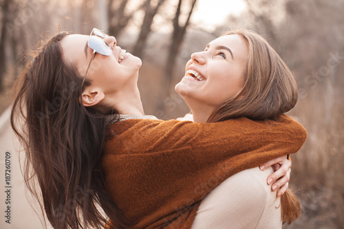 Two cute young women are hugging and laughing outdoors