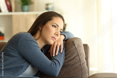 Sad woman looking trough a window sitting on a sofa