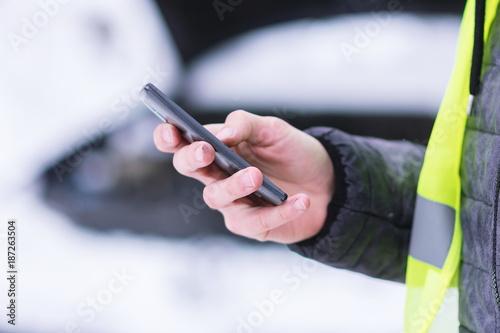 Man holding mobile phone and calling winter car services to help.