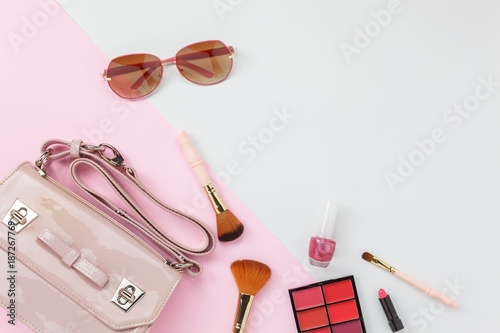 Table top view accessory of clothing women plan to travel in holiday background concept.Hand bag with many essential items cosmetic and sun glasses on modern white & pink paper.Duo with pastel tone.