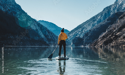 a woman with yellow plumber paddle surfing on a lake in a snowy mountain landscape
