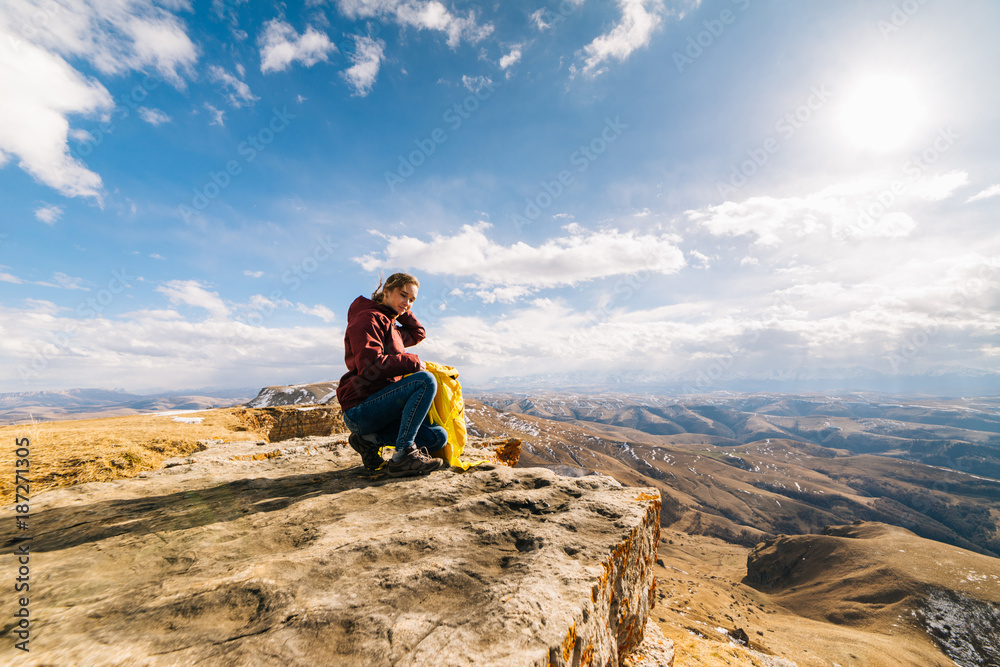 happy young girl sits on the edge of a cliff, travels along the Caucasian ridge