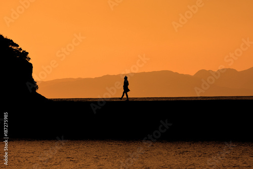 夕焼けの防波堤を歩く人のシルエット