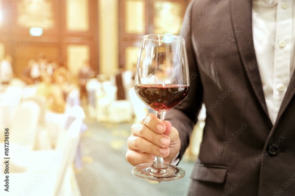 Close of of business man wearing suit holding a glass of wine in the company party with ray yellow light in the background. Concept and idea of business success, celebration party.