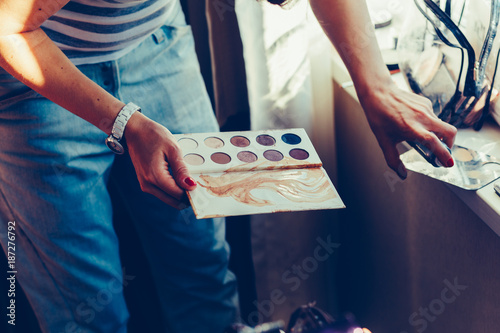 Female makeup artist with cosmetics at work close-up. Girl holding a white palette eyeshadow for makeup. Vintage tonted photo. photo