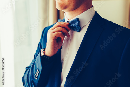 Closeup of a gentleman in an expensive suit wearing a blue tie, straightens his bow tie. Vintage tonted photo. photo