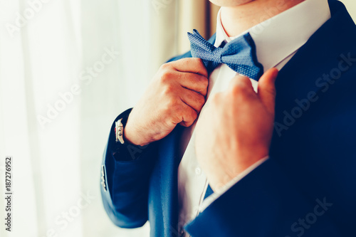 Fotografia, Obraz Closeup of a gentleman in an expensive suit wearing a blue tie, straightens his bow tie