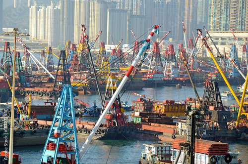 Commercial Barges with industrial freight cranes and marine shipping containers with city skyline, in Hong Kong Harbour, acting as a gateway to China