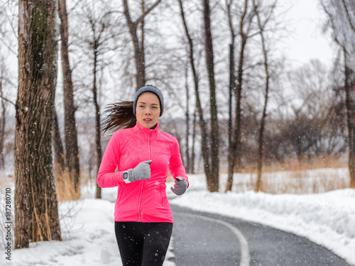 Winter running sport woman wearing jacket and smartwatch. Fit Asian runner jogging in winter forest doing outdoor run exercise. Active lifestyle. © Maridav