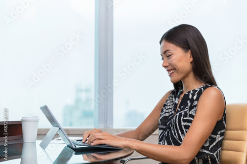 Asian business woman typing on laptop writing online working at office desk. Freelance remote work at home or customer service support. Businesswoman lifestyle.