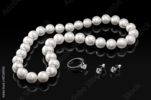 Luxury set white pearl necklace and jewelry with diamonds in ring and earrings on a black background with glossy reflection and blank template for your design or copy space your text 