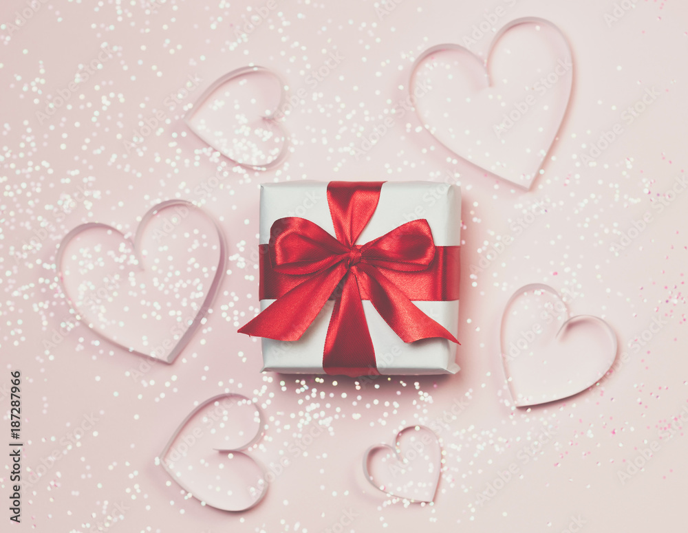 Gift box and paper hearts with sparkling glitter on pink background. Romantic st. Valentine's day concept of greetings. Top view, flat lay