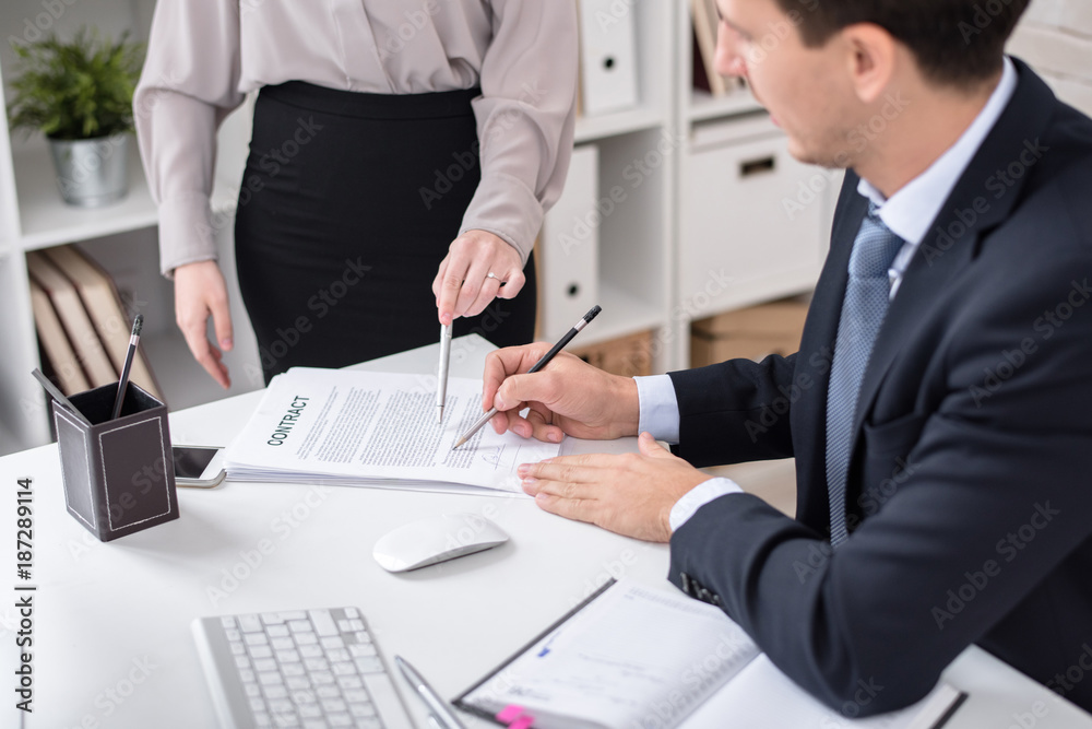 Portrait of successful business executive signing contracts with secretary at desk in modern office Portrait of successful business executive signing contracts with secretary at desk in modern office
