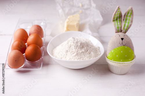 Ingredients for cooking dough, sweet baking. Bowl of flour, butter, eggs, baking molds and toy bunny, Easter spring background