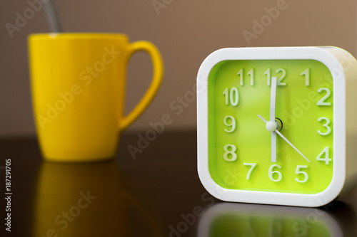 coffee time on morning before going work. Green alarm clock with yellow coffee cup on table. After wake up will drink hot beverage before going to work.