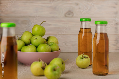 Green apples in a lilac plate and a bottle of apple juice on a wooden light background.
