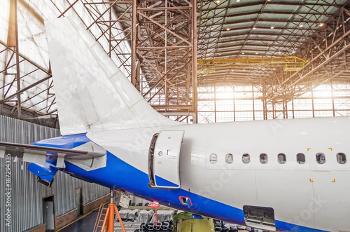 Passenger aircraft on maintenance, a view of the tail and the rear of the fuselage in airport hangar.