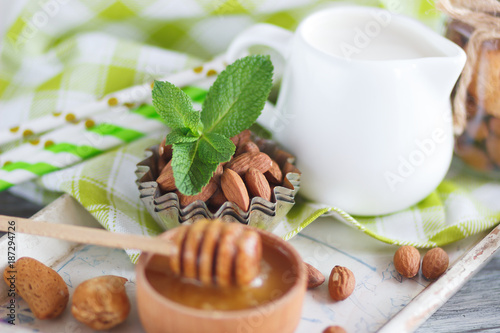 Honey in the wooden bowl, mint leaves, almonds and jar with milk on the wooden tray