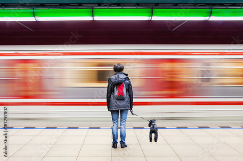 Lonely woman with dog at subway station platform with blurry moving train in background