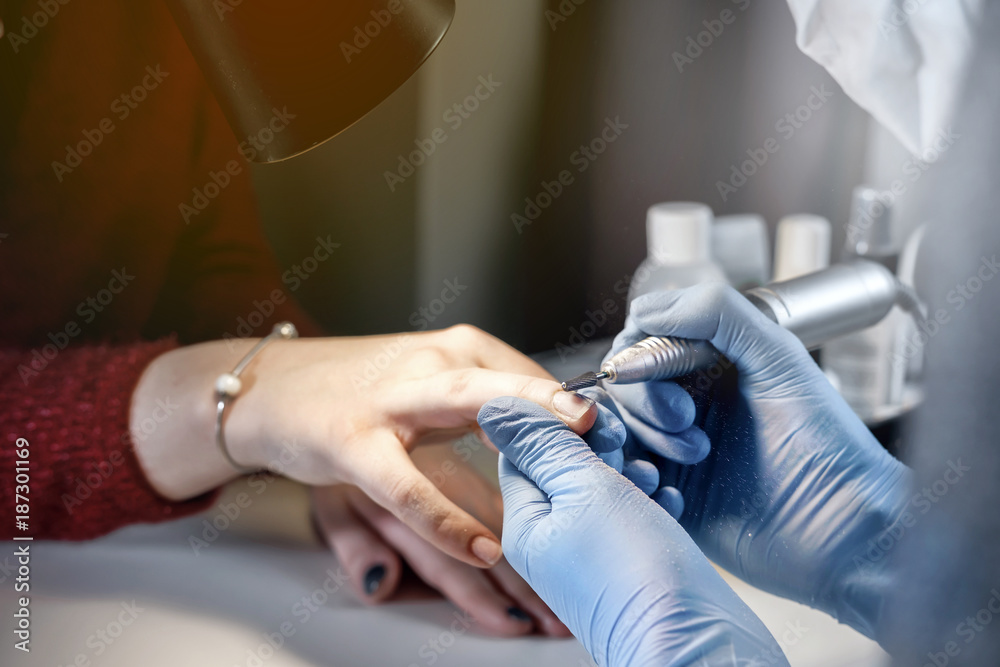 Fototapeta premium girl does manicure, professional manicure in the salon, removal of gel varnish with help of apparatus, Hands in rubber gloves, protective face mask, manicure of beautiful female hands, working process