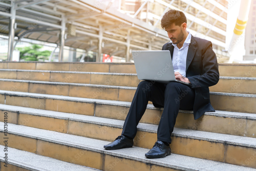 Handsome young manager working on laptop computer while sitting outdoors on the stairs, concept of technology and communication.. Handsome young manager working on laptop computer while sitting outdoors on the stairs, concept of technology and communication..
