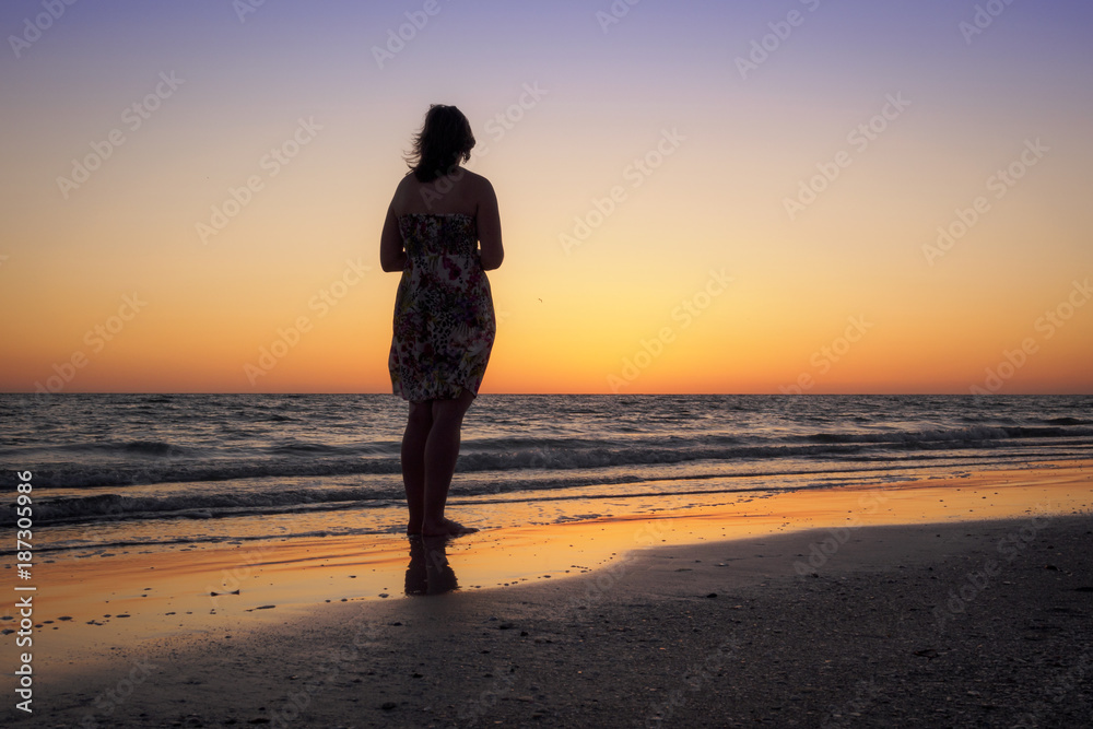 Sillhouette of a beautiful woman admiring the sunset on a beach in Florida