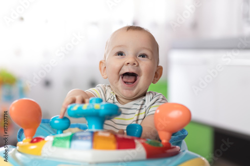 Portrait of baby in baby walker. Expressive child plays toys.