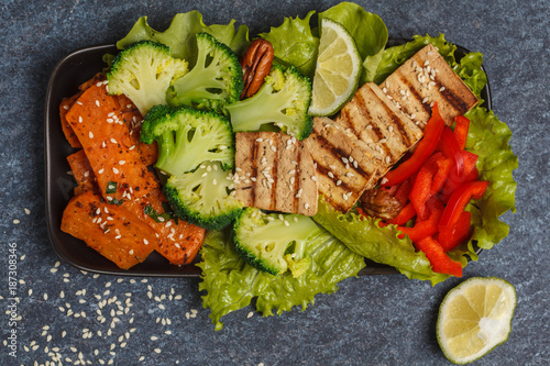 Vegetarian asian salad with sweet potato, grilled tofu, broccoli and pecan. Healthy vegan food concept. Top view, dark background, copy space.
