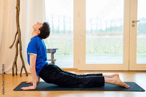 Man practicing yoga indoors in a retreat space doing Upward facing dog pose - urdhva mukha svanasana