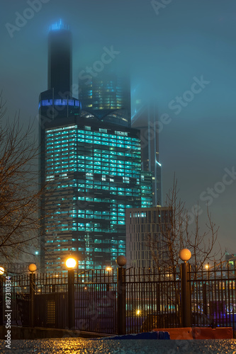 the tops of modern skyscrapers in the night fog photo