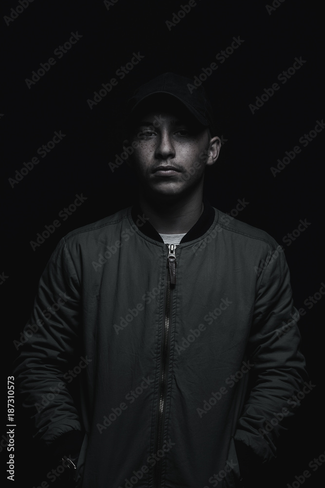 teen boy posing with black cap and bomber jacket in front of black background teen boy posing with black cap and bomber jacket in front of black background