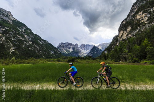 Mountain biking woman and young girl along river in Dolomites, Italy