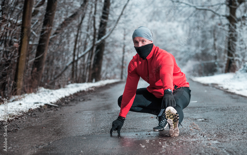 Winter running exercise, runner stretching on road in snowy forest Winter running exercise, runner stretching on road in snowy forest