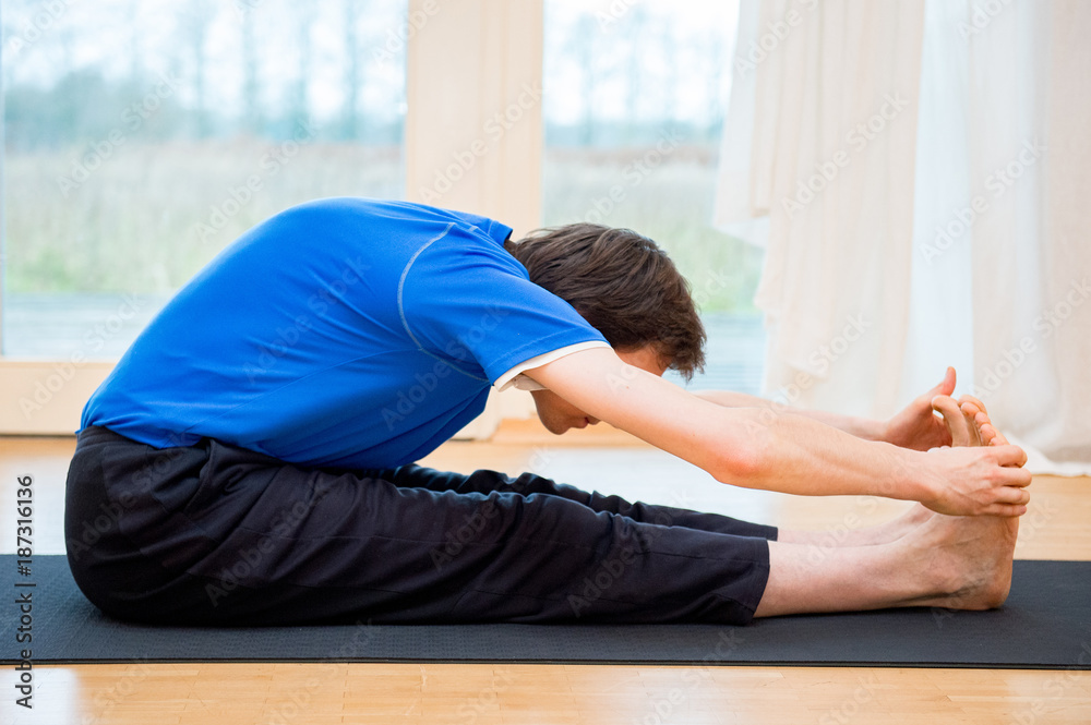 Man practicing yoga indoors in a retreat space doing Seated Forward Bend Pose - Paschimottanasana Man practicing yoga indoors in a retreat space doing Seated Forward Bend Pose - Paschimottanasana