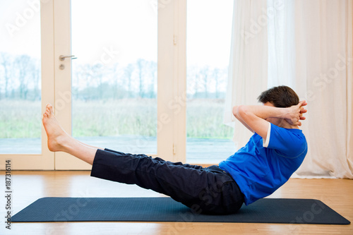 Man practicing yoga indoors in a retreat space doing Half Boat Pose - Ardha Navasana