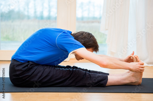 Man practicing yoga indoors in a retreat space doing Seated Forward Bend Pose - Paschimottanasana